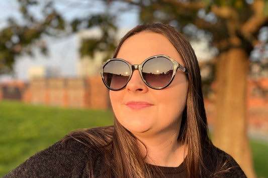 Woman in a park wearing sunglasses with 100% UV protection.