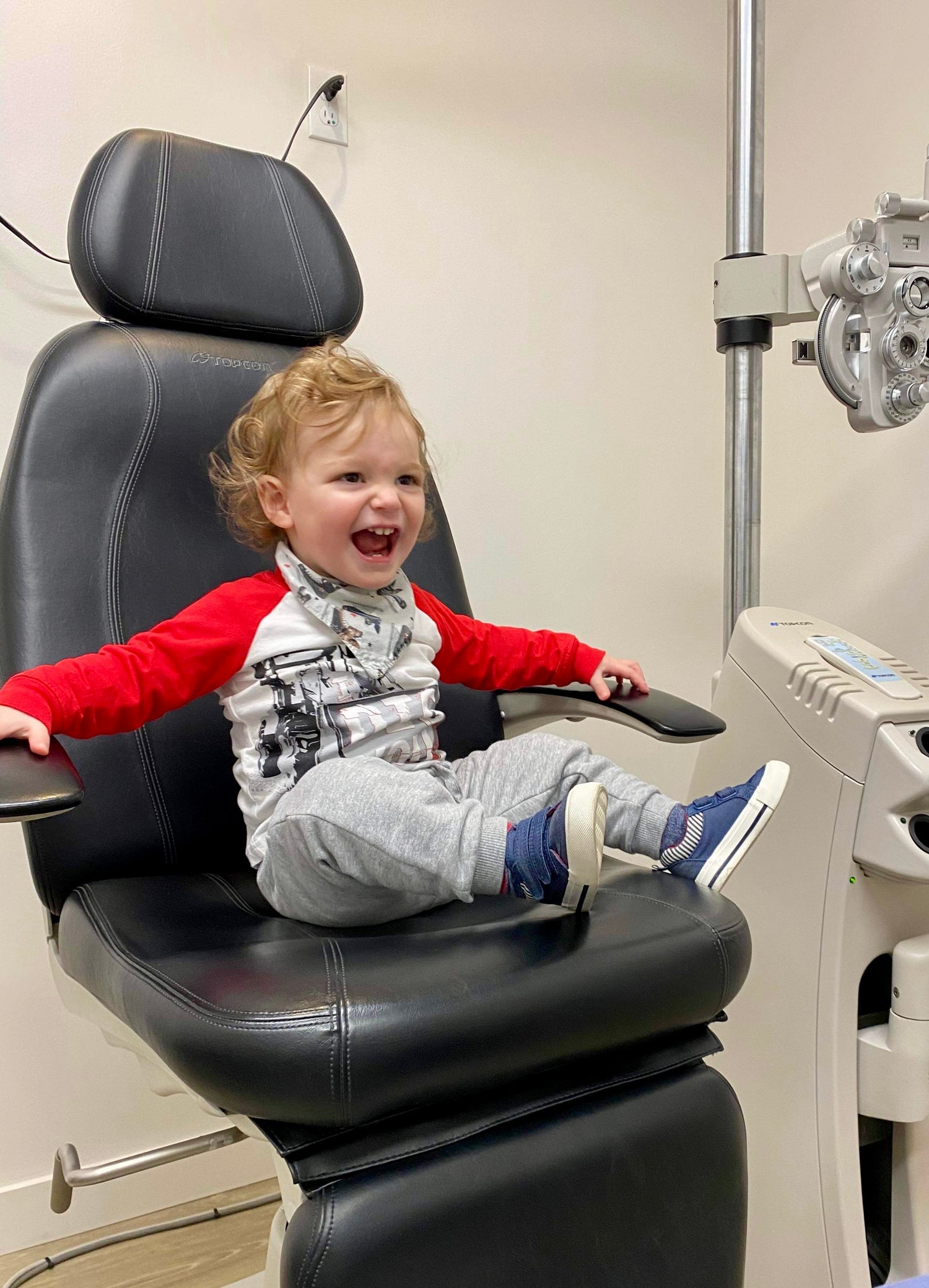 Infant boy sitting in an eye exam chair, laughing and looking excited.