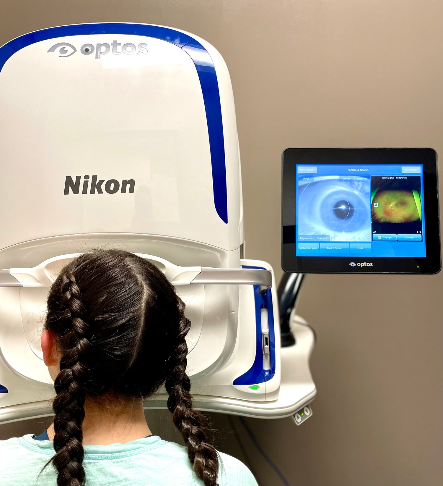 Child facing away, looking into a large camera labelled Optos Nikon. A screen next to her shows her eye picture.