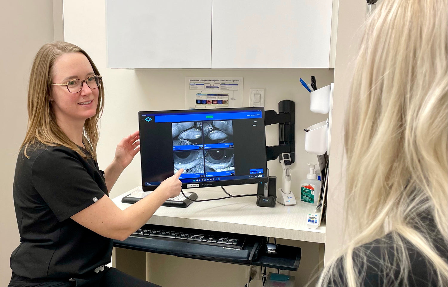 Dr Tracy Voegeli pointing to close up of eyelid glands on a screen. Someone sitting across from her while she explains.