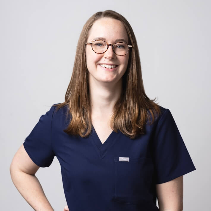 Dr Tracy Voegeli in blue scrubs, posed with one hand on hip, smiling.