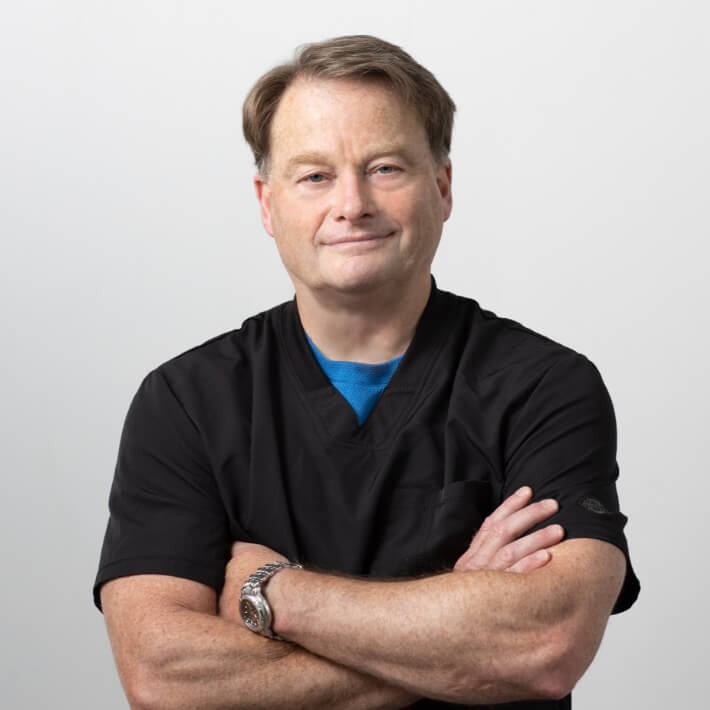 Dr Carl Davis in scrubs, arms folded, smiling.