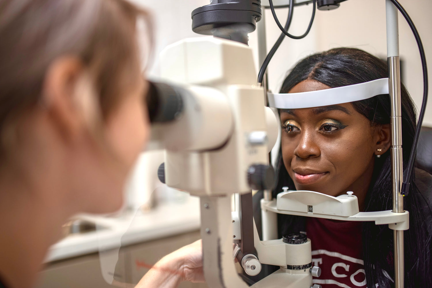 Optometrist looking through microscope towards a patient's eye. Patient is smiling.