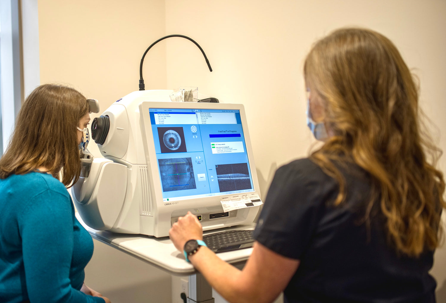 Woman positioned and looking into an OCT machine. A technician sitting next to her looking at screen and recording scans.