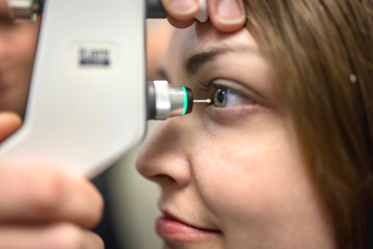 Close up of a woman having their eye pressure checked by a small instrument holding a probe in front of her eye.