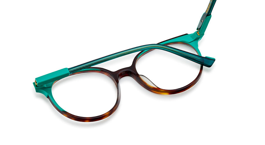 Women’s prescription eyewear: A close-up view of an oval tortoise front with clear turquoise temples. Part of the hinges are made of a solid plastic the same shade. 