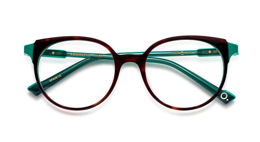 Women’s prescription eyewear: A front view of an oval tortoise front with clear turquoise temples. Part of the hinges are made of a solid plastic the same shade. The Etnia insignia located on the inside of the temple tips.